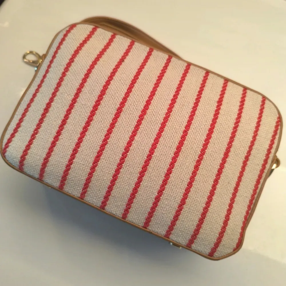 Snygg axelväska från Valentino med röd- och vitrandigt mönster. Väskan har en justerbar axelrem i beige och en praktisk dragkedja upptill. Perfekt för att ge din outfit en stilren touch.. Laukut & Käsilaukut.