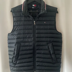 Mörkblå dunväst från Tommy Hilfiger - Snygg mörkblå dunväst från Tommy Hilfiger med dragkedja och quiltad design. Hör av dig vid frågor. Alltid snabba svar! Skickar inom 1 dag!
