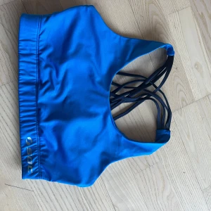 Blå sport-bh från soc - Säljer en blå sport-bh från soc med snygga korsade band i ryggen. Perfekt för träning och ger bra stöd. Den har en elastisk kant nedtill för extra komfort. Liten i stl.