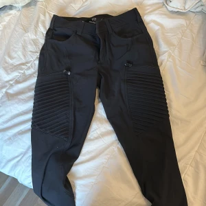 Svarta Pusher Jeans från RVRC - Nypris runt 1,2 tusen men har inte användning för dem. Snygga svarta Pusher Jeans från RVRC med  ribbade detaljer på benen och dragkedjor vid fickorna. Perfekta för en stilren och modern look. Galet bra revolution race friluftsbrallor, stryktåliga, bra att jobba och ha ute i naturen 