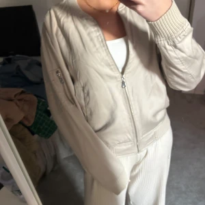 Beige bomberjacka från The Black Label Collection - Säljer en stilren beige bomberjacka från The Black Label Collection. Jackan har en dragkedja framtill och ribbade muddar vid ärmslut och nederkant. Perfekt för en avslappnad look.