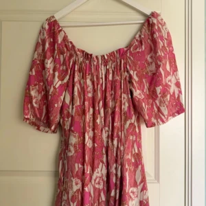 American eagle rosa långklänning - Charmig rosa långklänning med blommigt mönster och offshoulder-design. Klänningen har korta ärmar och en luftig passform, perfekt för varma dagar.