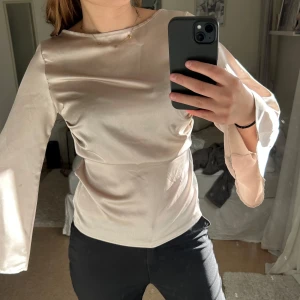 Beige långärmad blus - Säljer en elegant beige blus med långa ärmar och en lätt glansig finish. Blusen har en lös passform och är perfekt för en stilren look. Den är tillverkad i ett mjukt och bekvämt material. Från bohoo.
