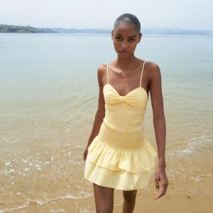 Gul rutig klänning med volang - Jättefin gul klänning från Zara som är helt slutsåld. Storlek M. Den har en volangdetalj och en stor rosett på baksidan. Perfekt för soliga dagar! Den är helt oanvänd och har lappen kvar❣️