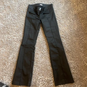 Svarta bootcut byxor - Snygga svarta bootcut byxor med låg midja och två knappar fram. Byxorna har en stilren design med fickor och är perfekta för en trendig look.