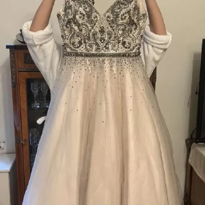 Bal/fest klänning i ljus beige med paljetter  - Elegant vit långklänning med v-ringad design och detaljerade paljetter på överdelen. Klänningen har en vacker omlott-look och är perfekt för festliga tillfällen som tex balen. 