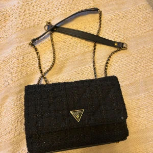 Svart axelväska från Guess -  svart axelväska från Guess med kedjedetaljer och en justerbar axelrämm , den är sparsamt andvänd och i mycket bra skick