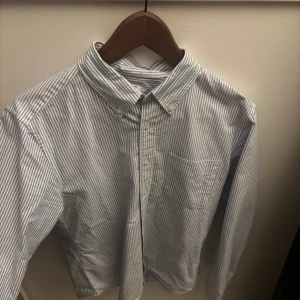 Blå- och vitrandig skjorta från Uniqlo - Säljer en stilren blå- och vitrandig skjorta från Uniqlo. Skjortan har en klassisk krage och knappar framtill samt en bröstficka. Perfekt för en avslappnad men ändå uppklädd look. Bara att höra av dig ifall du har några frågor, priset är diskuterbart🤩🤝