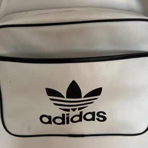 Vit axelväska från Adidas - Vit väska från Addidas. I bra skick och går lätt att torka av. Säljs pga att den inte används