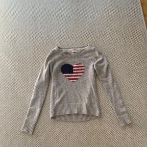 Grå stickad tröja Hilfiger Denim M - Säljer denna stickade tröja från Tommy hilfiger med ett hjärta i mitten. Tröjan är i bra skick förutom att det finns ett hål i ena armen ( se bild) men inget annat. Tröjan är i storlek M men är liten i storleken skulle jag säga så passar även S och Xs.