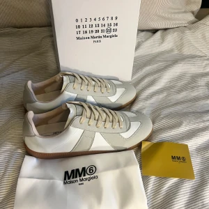 Maison Margiela gats  - Maison Margiela sneakers i vitt och ljusgrått skinn och mocka, med beige snörning och klassisk gummisula. Snygg minimalistisk design med diskreta detaljer och ikonisk Margiela-etikett på plösen. Perfekta för dig som gillar stilrena och trendiga sneakers. OBs lnte 0rglnal 