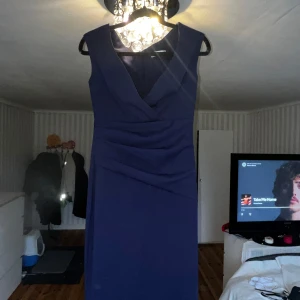 Mörkblå omlottklänning i storlek 36 - Snygg mörkblå omlottklänning i figurnära modell med v-ringning och draperad front. Ärmlös design och klassisk siluett som passar perfekt när du vill känna dig extra fin. Tillverkad i ett mjukt och följsamt material. (Frakt betalar köparen)