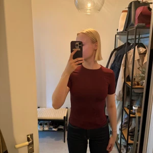 Vinröd topp från H&M, XS - En enkel och stilren vinröd tight T-shirt från H&M i storlek XS. Modellen är figurnära med korta ärmar och rund halsringning. Perfekt att matcha med jeans eller kjol. Materialet är mjukt och stretchigt, vilket gör den riktigt skön att bära.