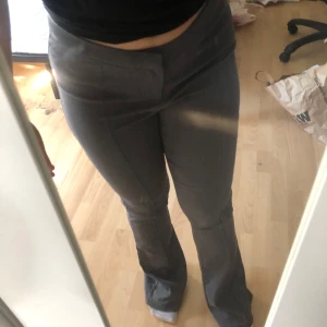 Grå bootcut kostymbyxor H&M Divided - Snygga grå kostymbyxor från H&M Divided i storlek 38. Byxorna har bootcut-ben och hög midja, med en stilren look och pressveck framtill. Perfekta för dig som gillar en klassisk men trendig vibe. Materialet är mjukt och stretchigt för extra komfort.