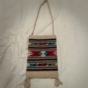 Beige väska med mönster och tofsar - Säljer en beige axelväska i stickat material med färgglatt mönster.