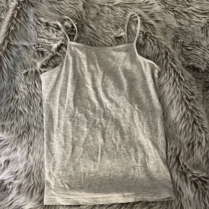 Grå linnetopp från H&M - Säljer en enkel och stilren grå linnetopp från H&M med smala axelband!! Toppen är ärmlös och har en rak passform, perfekt att matcha ihop med en massvis med outfits!!☺️ Tillverkad i mjuk bomull för en bekväm känsla hela dagen!! Knappt använd och mycket bra kvalitet! Den är lite skrynklig men det stryker jag såklart till innan leverans så den blir slät och fin!😊Det är bara att höra av sig för frågor, mått eller fler bilder!!🥰
