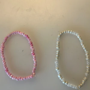 Två pärlfotarmband i rosa och vitt - Säljer två handgjorda fotarmband med glansiga pärlor. Ett fotarmband har pärlor i olika rosa nyanser och det andra har pärlor i vitt och silver. Perfekta accessoarer för att ge din outfit en söt och färgglad touch.  30kr för båda