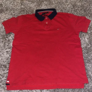Röd pikétröja från Tommy Hilfiger - Röd pikétröja från Tommy Hilfiger med klassisk marinblå krage och små knappar. Köpt på Hanzens, auktoriserad återförsäljare i Umeå!