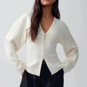 Vit kofta med knappar från Gina Tricot - Säljer en stilren vit kofta från Gina Tricot i storlek XS. Koftan har v-ringning, klädda knappar framtill och är tillverkad i ett mjukt, stickat material. Lite nopprig och lite uttöjd i knappen högst upp då min byst varit lite stor för tröjan.