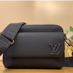 Svart axelväska från Louis Vuitton - Snygg svart axelväska från Louis Vuitton i stilren design med bred justerbar axelrem och präglad LV-logga framtill. Väskan är tillverkad i mjukt skinn och har ett stort huvudfack med dragkedja samt en praktisk ytterficka. Perfekt för dig som vill ha en clean och lyxig look.