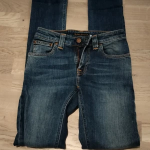 Blå skinny jeans från Nudie Jeans - Snygga blå jeans från Nudie Jeans med klassisk femficksdesign och orangea kontrastsömmar. Modellen är skinny fit med normal midja och har Nudie Jeans signaturbroderi på bakfickorna. Perfekta till sneakers eller boots.