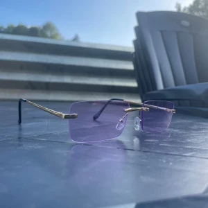 Lila rektangulära glasögon med gulddetaljer - Säljer ett par stilrena glasögon med rektangulära lila glas och tunna guldfärgade bågar. Glasögonen har näskuddar för extra komfort och svarta skalmar. Perfekta brillor för dig som vill sticka ut med en modern vibe.