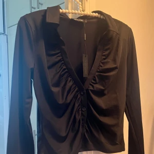 Ny svart långärmad festtopp - Helt ny med prislapp!  Storlek S Formar kroppen fint. Säljer även i brunt.  Slits längst ner på ärmen, se sista bilden. Kan mötas upp i Stockholm. Bara att höra av er om ni har några frågor<3