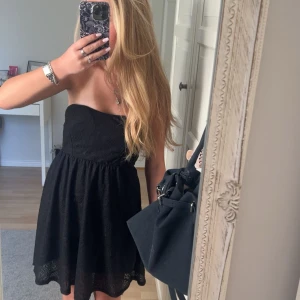 Svart axelbandslös spetsklänning - Supersöt svart kortklänning med axelbandslös design och öppen rygg. Klänningen har ett fint spetslager över hela tyget och en liten cut-out detalj bak. Klänningen är vadderad💗💗💫