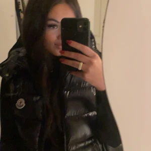 Moncler väst  - Säljer en svart, glansig dunväst från Moncler med avtagbar huva och dragkedja framtill. Västen har två fickor med dragkedja. Storlek- S men passar även M. Äkthetsbevis och dokument medskickas. Pris kan diskuteras vid snabba affär. 