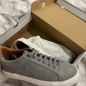 Oanvända gråa sneakers från Zara (Man) - Stilrena grå sneakers från Zara med vita sulor och grå snörning. Insidan är fodrad i ljusbrunt för en snygg kontrast. Perfekta för dig som gillar minimalistisk och clean stil. Storleken är 43 
