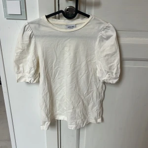 Vit puffärm topp från Vero Moda - Säljer en stilren vit topp från AWARE by Vero Moda i storlek XS. Toppen har korta puffärmar och rund halsringning. Tillverkad i mjuk bomull, perfekt för en clean och enkel look. Passar dig som gillar minimalistisk stil.