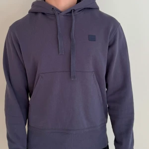 Mörkblå hoodie Acne Studios Ferris Face - Snygg mörkblå hoodie från Acne Studios, modell Ferris Face. Tröjan har huva med snörning, magficka och den klassiska Face-loggan på bröstet. Tillverkad i 100% bomull för en skön och avslappnad känsla.