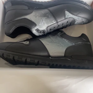 Louis Vuitton sneakers stl 44 - Snygga svarta Louis Vuitton sneakers i skinn med grå paneler och ikoniskt LV-monogram. Skorna har kraftig sula, rund tå och svarta snören. Perfekta för dig som vill sticka ut med exklusiv streetstyle och lyxig känsla.