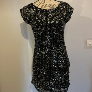 Svart paljettklänning med öppen rygg - Supersnygg svart kortklänning täckt av glittriga paljetter. Klänningen har korta ärmar och en riktigt snygg öppen rygg med knyt i nacken.  