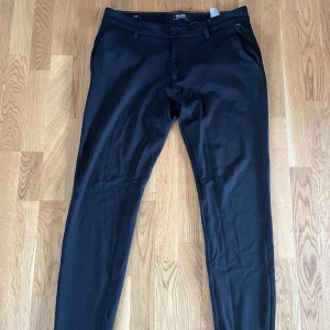 Svarta kostymbyxor  - Svarta kostymbyxor från ONLY & SONS med smal passform och klassisk design. Byxorna har sidfickor, hällor för bälte och bakfickor. Slitage mellan benen men går enkelt att laga!