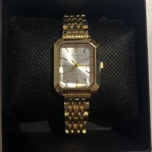 Guldfärgad klocka från Ximili - Elegant guldfärgad klocka från Ximili med rektangulär urtavla och kvartsverk. Klockan har en stilren design med guldfärgad länkarmband och tydliga markeringar på urtavlan. Perfekt för att ge en touch av lyx till din stil.