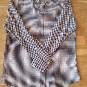 Rutig skjorta från Ralph Lauren - Klassisk rutig skjorta från Ralph Lauren i blått och vitt. Skjortan har lång ärm, knappar framtill och en liten broderad logga på bröstet. Perfekt för en stilren och avslappnad look.