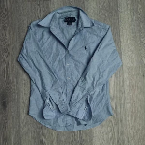 Ljusblå  skjorta  från Ralph Lauren - Klassisk blå skjorta från Ralph Lauren med broderad logga på bröstet. Är i storlek L i barnstorlek vilket motsvarar en Xs🔥