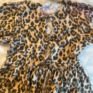 Leopardmönstrad tröja Gina Tricot - Cool tröja från Gina Tricot i leopardmönster med beige och svarta toner. Tröjan har korta puffärmar, knytning fram och rynkad midja för en snygg siluett. Perfekt för dig som vill sticka ut med en trendig look.