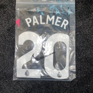 Chelsea Palmer #20 bortatröja Nike S - Chelsea FC bortatröja med Palmer och nummer 20 på ryggen. Svart och grått rutmönster, rosa detaljer på ärmslut och klubbmärke, samt gul insida på ärmarna. Tillverkad i lätt och ventilerande material, perfekt för match eller supporterliv.