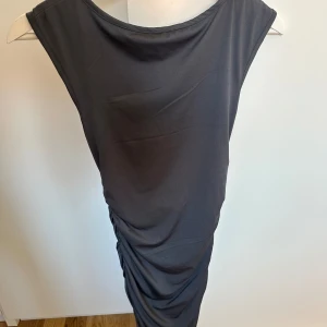Mörkgrå klänning från SHEIN XS - Snygg mörkgrå klänning från SHEIN i stretchigt polyestertyg. Klänningen är ärmlös med draperad effekt längs båda sidorna och har en djup, öppen rygg. Perfekt för dig som gillar minimalistisk och stilren look.