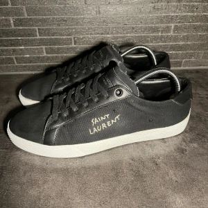 Svarta Saint Laurent sneakers - Svarta sneakers från Saint Laurent med vit logga broderad på sidan. Skorna är i storlek 43. Skick är mycket bra 9/10. OG/tillbehör inget därav det lägre priset. Givetvis är dom ÄKTA vilket garanterar. Obs sulkräm har använts 