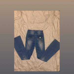 Blå bootcut jeans med detaljer - Snygga blå bootcut jeans i storlek S med hög midja. Snygga detaljer framtill och coola bakfickor med nitar, mönster och knappar. Klassisk femficksdesign med bälteshällor för en stilren finish. Perfekta för en trendig vardagslook. Obs! Jag har råkat spilla lite nagellim på byxorna, har försökt få bort det men det sitter kvar. Vilket förstörde lite helheten men viktigt att veta, därav priset!