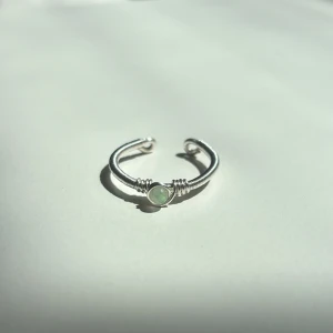 New Jade Ring - Denna ring är tillverkad för hand med rostfri ståltråd som gör den både slitstark och rostfri. Ringen är justerbar för att passa perfekt på de flesta fingrar och pryds av pärlor i äkta New Jade – vilket ger ett naturligt och harmoniskt uttryck. Den är dessutom vattentålig och passar utmärkt för vardagsbruk.