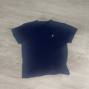 Mörkblå t-shirt från Polo Ralph Lauren - Snygg mörkblå t-shirt från Polo Ralph Lauren med klassisk passform och broderad logga på bröstet. Tillverkad i mjuk bomull och har rund halsringning samt korta ärmar. Perfekt för en clean och stilren look.