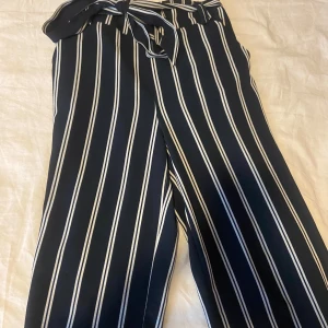 Randiga vida byxor med knytband - Snygga mörkblå byxor med vita vertikala ränder och knytband i midjan. Byxorna har en wide fit och hög midja, vilket ger en chill och trendig look. Perfekta att styla med en enkel topp eller hoodie.