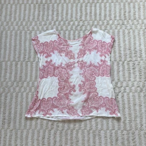 Vit och röt blus från Rabalder - Supersöt blus från Rabalder i vitt med detaljerat rött paisleymönster. Modellen har korta ärmar och rund halsringning. Tunt och luftigt material som känns skönt mot huden. Perfekt för dig som gillar romantiska och unika prints.