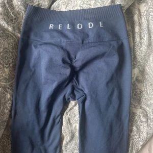 Mörkblå tights från Relode - Säljer ett par mörkblå tights från Relode med hög midja och bred resår. De är stretchiga och sitter tight, perfekta för träning eller chill. Materialet är mjukt och följsamt, och loggan är tryckt framtill i midjan. väldigt bra skick inga defekter