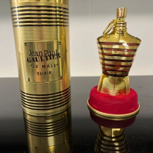 Jean Paul Gaultier Le Male Elixir - Exklusiv parfym i guldig metallflaska formad som en manlig torso med svarta ränder. Kommer i en matchande guldig burk med märkets logga och röd sammetsbas. En riktig statement-doft för dig som gillar lyxig design.