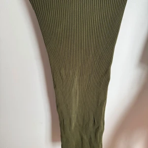 Olivgrön ribbad långkjol från H&M - Säljer en olivgrön, ribbad långkjol med tight passform. Kjolen är stretchig och sitter snyggt längs kroppen, perfekt för dig som gillar en enkel men trendig look. Midjan är normal och materialet känns mjukt och bekvämt. Ej några fläckar på kjolen, det är spegeln som är  smutsig🙈